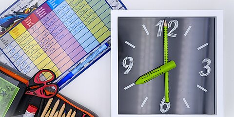 Eine Uhr, ein Stundenplan und ein Federpenal mit Stiften und Schere